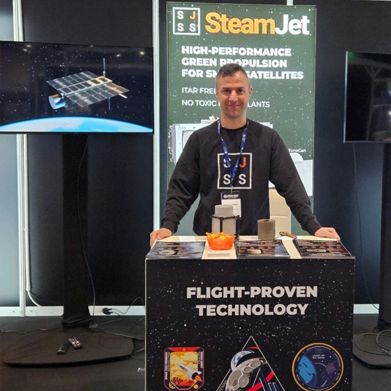 A wide shot of Steamjet Space Systems exhibiting at a space conference in March 2026 with a TV screen which is displaying their satellite animation produced by Sound Motive.